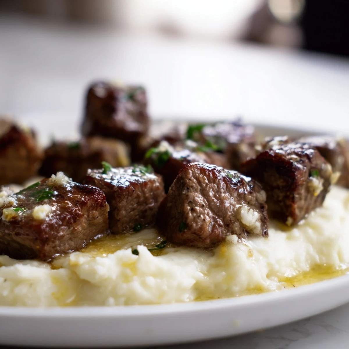 A close-up of golden seared Garlic Butter Steak Bites with Mashed Potatoes, drizzled with fresh garlic butter and parsley.