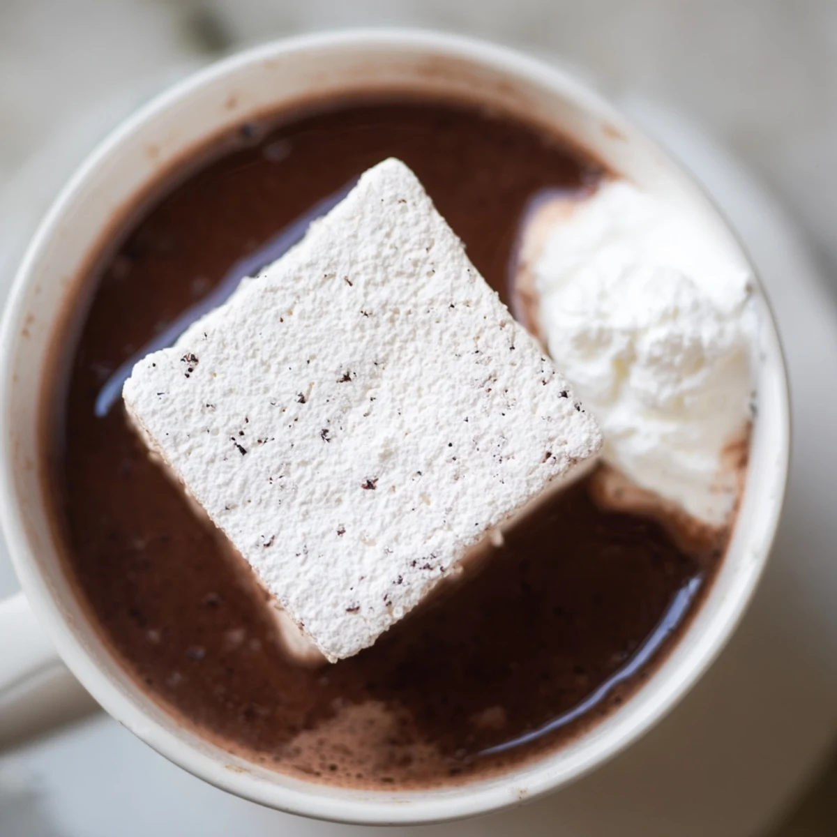 Homemade vanilla bean marshmallow floaters melting into creamy hot chocolate in a cozy mug.