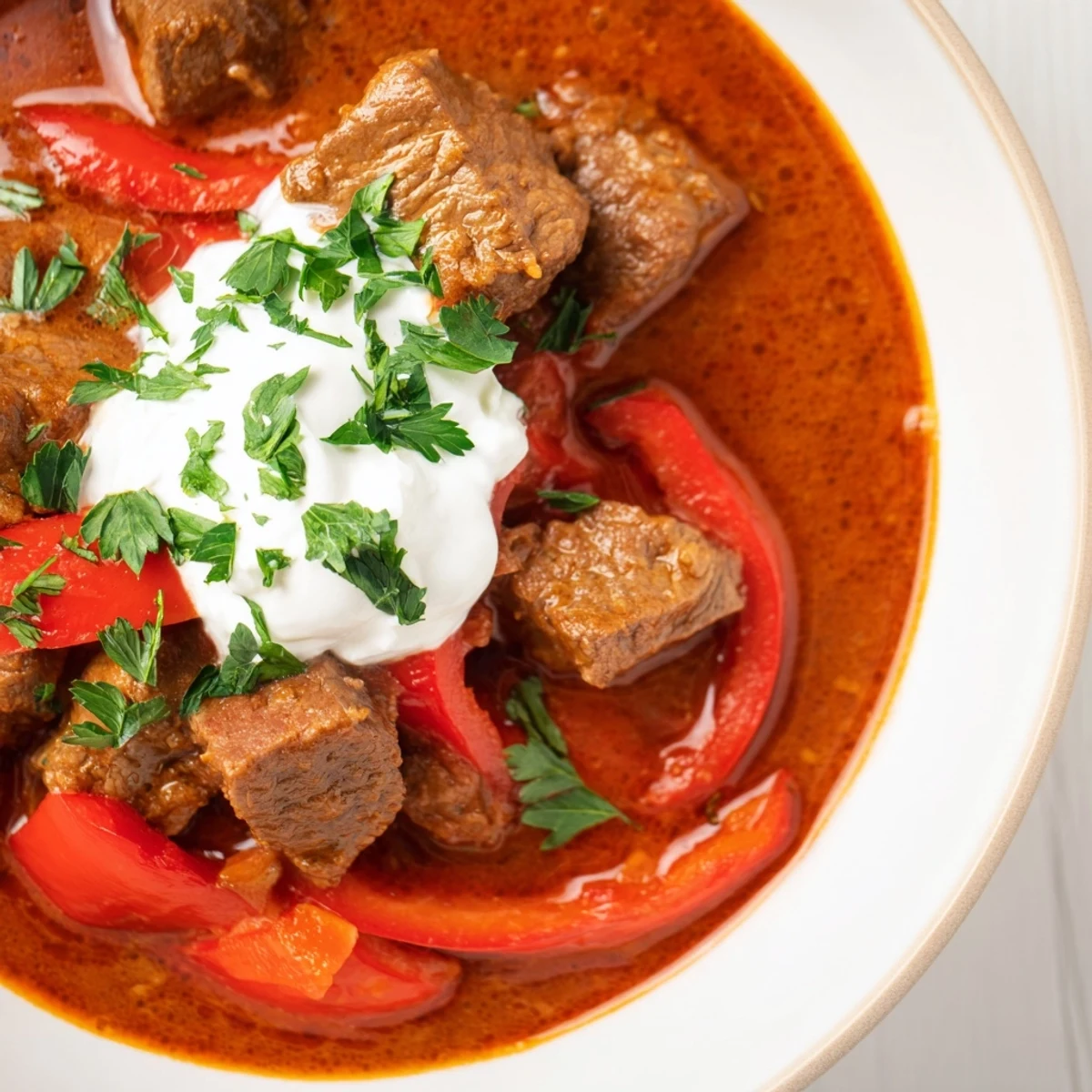 Close up of rich beef goulash with bell peppers in a rustic bowl, paprika infused sauce glistening, ready to be scooped with crusty bread.