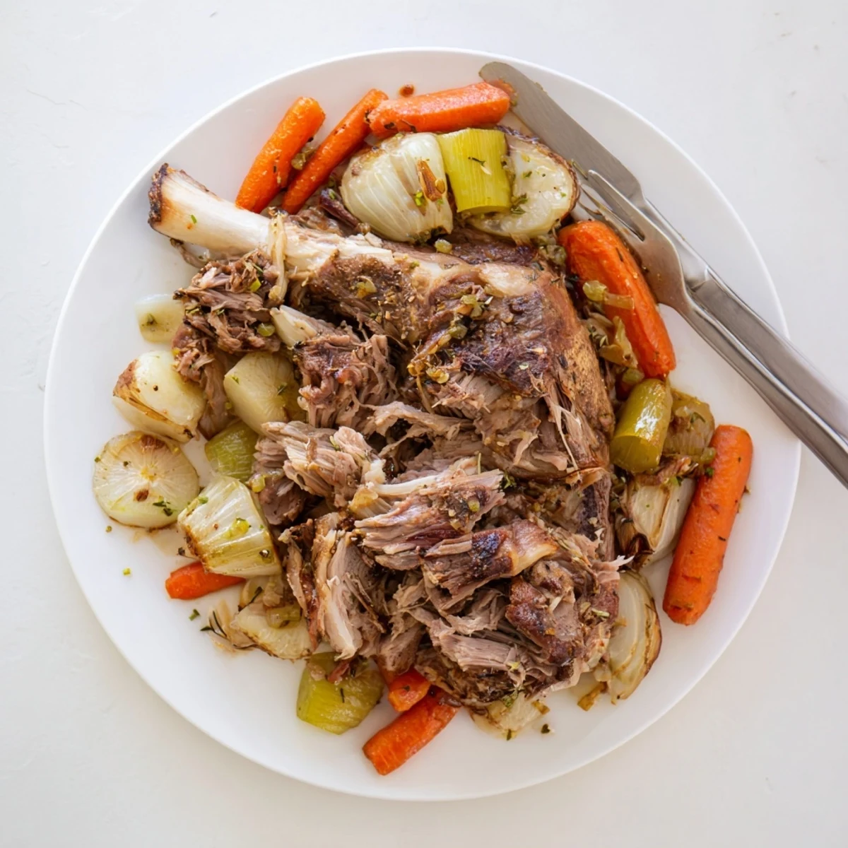 A close-up of Slow Cooked Lamb Shoulder with Garlic Herbs, showing tender, shredded meat and aromatic roasted vegetables in a rich sauce.