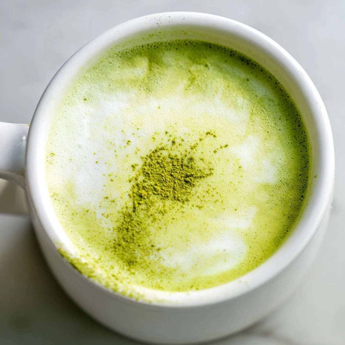 Homemade Shamrock Green Matcha Latte with Honey topped with edible gold flakes, served alongside a flaky pastry on a rustic table.