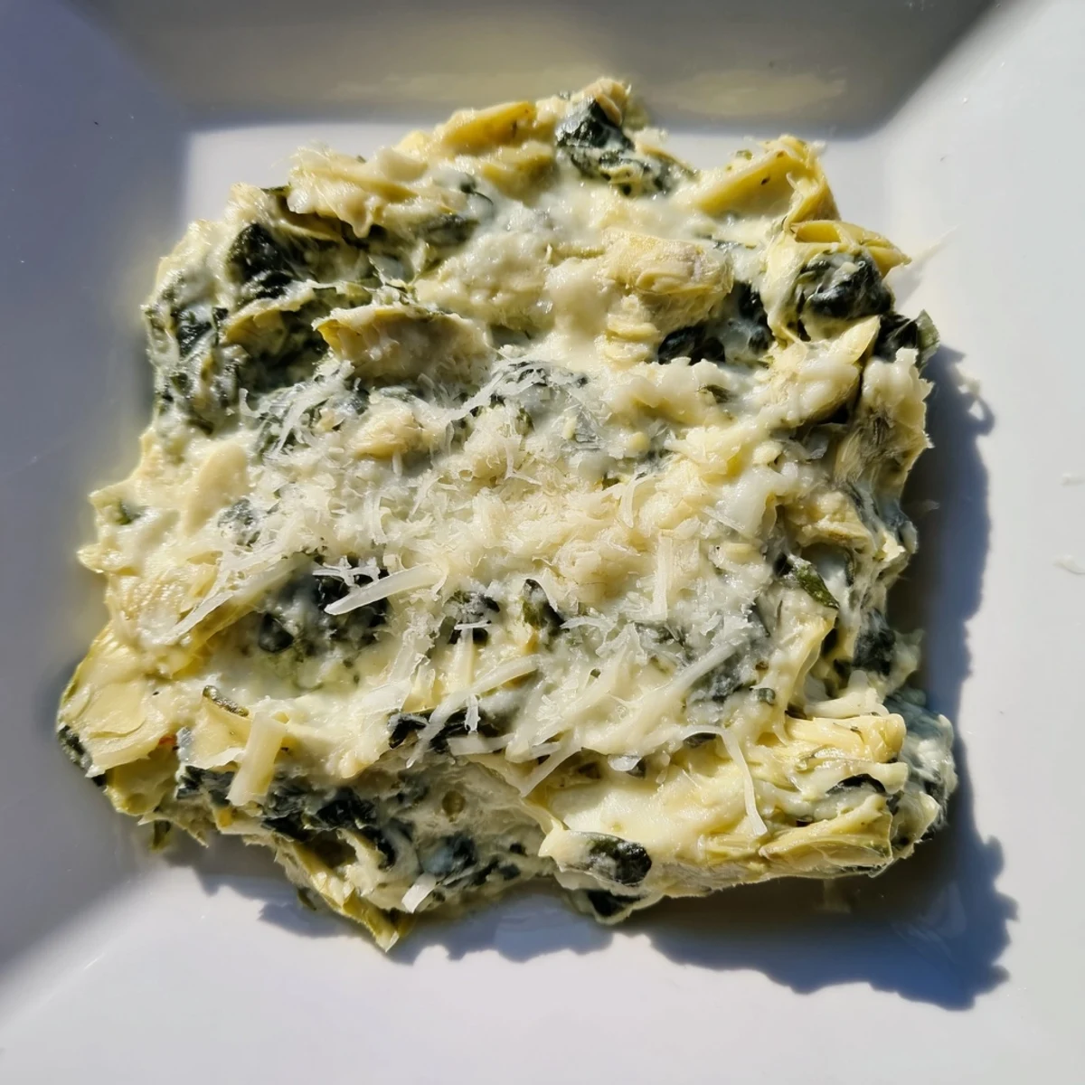 Creamy Spinach and Artichoke Dip is spooned from a baking dish onto a piece of crusty bread.