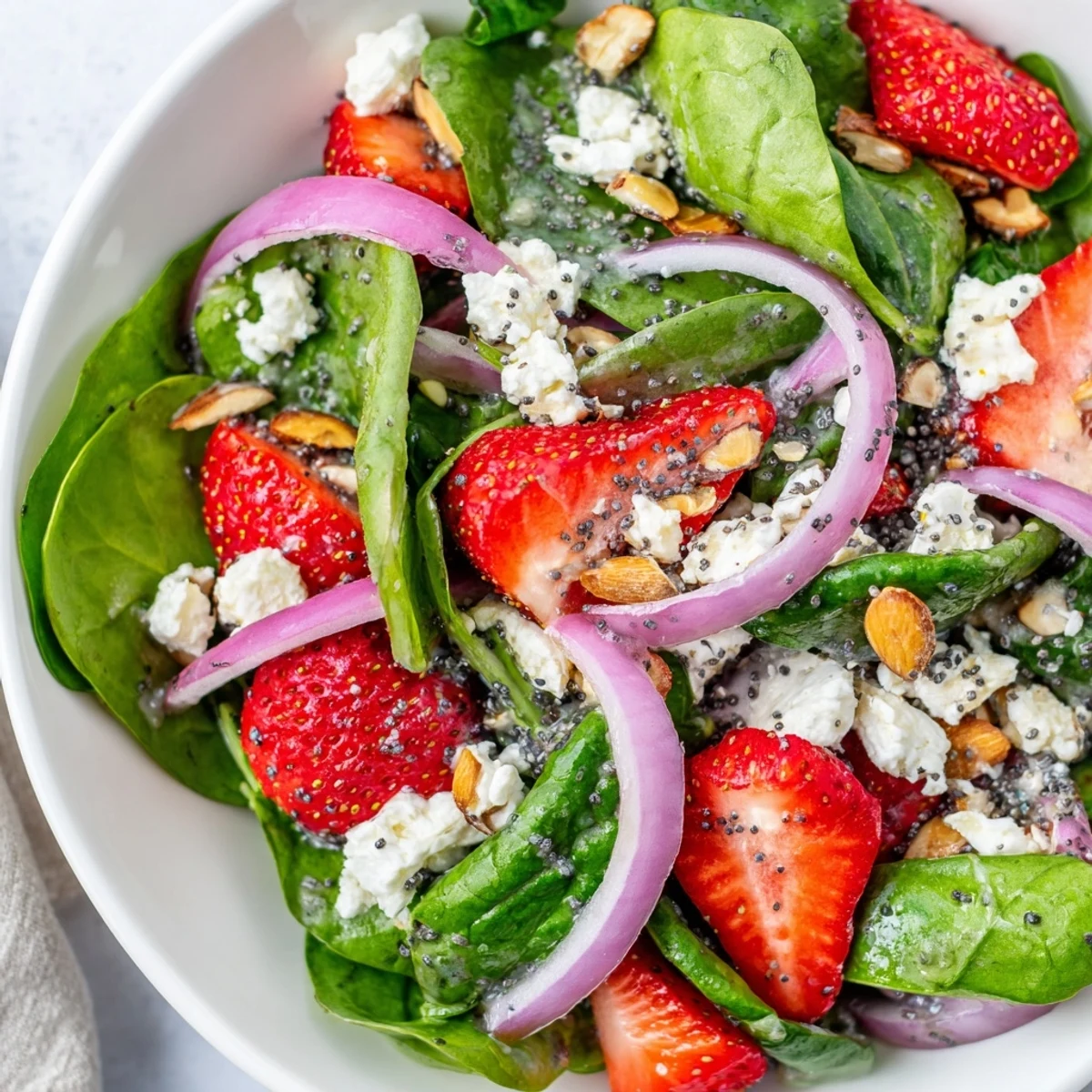 Fresh baby spinach leaves topped with sliced strawberries, crumbled feta, and toasted almonds for a colorful spring salad.  