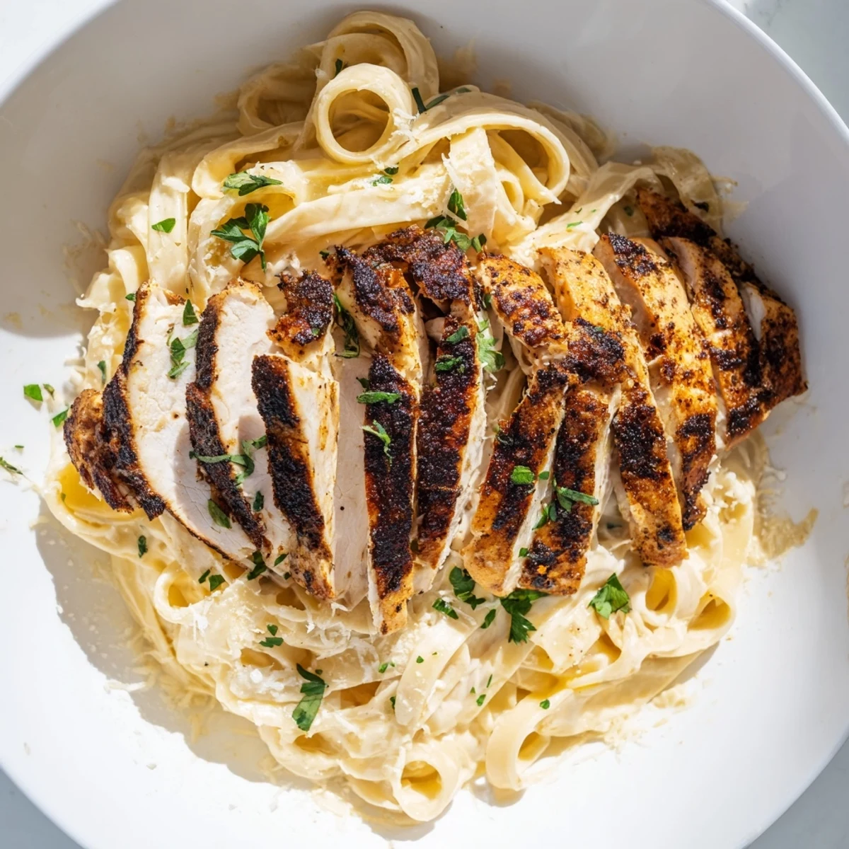 Rich Cajun Blackened Chicken Alfredo steaming in a shallow bowl, highlighting the contrast of dark spices and velvety white Alfredo sauce.