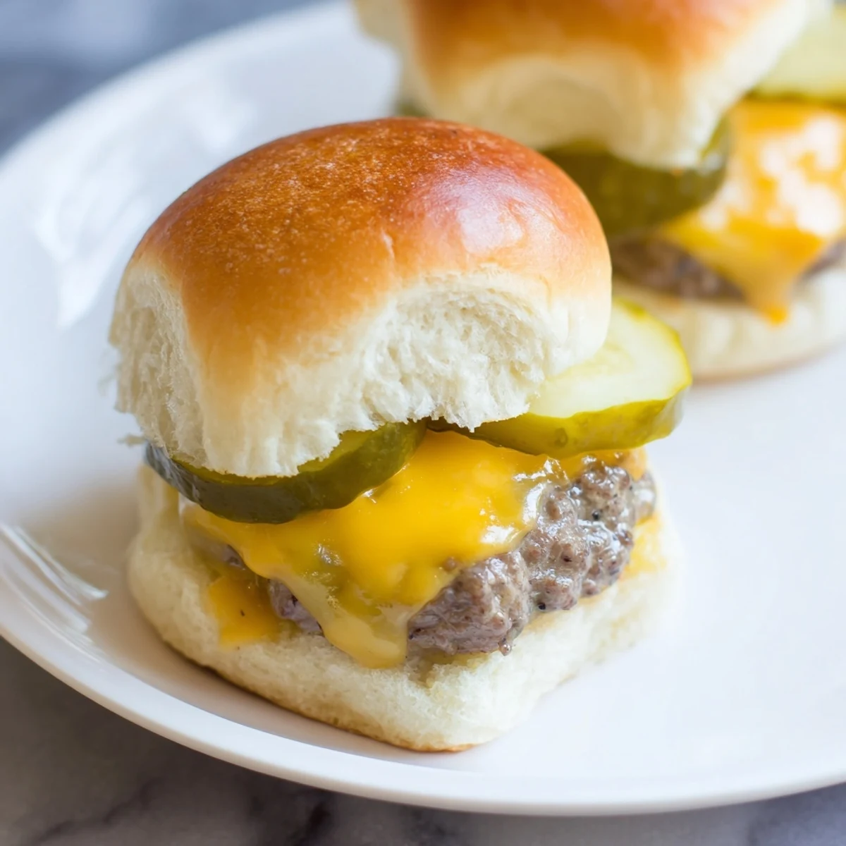 Close-up of mini beef burgers topped with cheese and pickles, juicy patties and toasted buns on a platter.