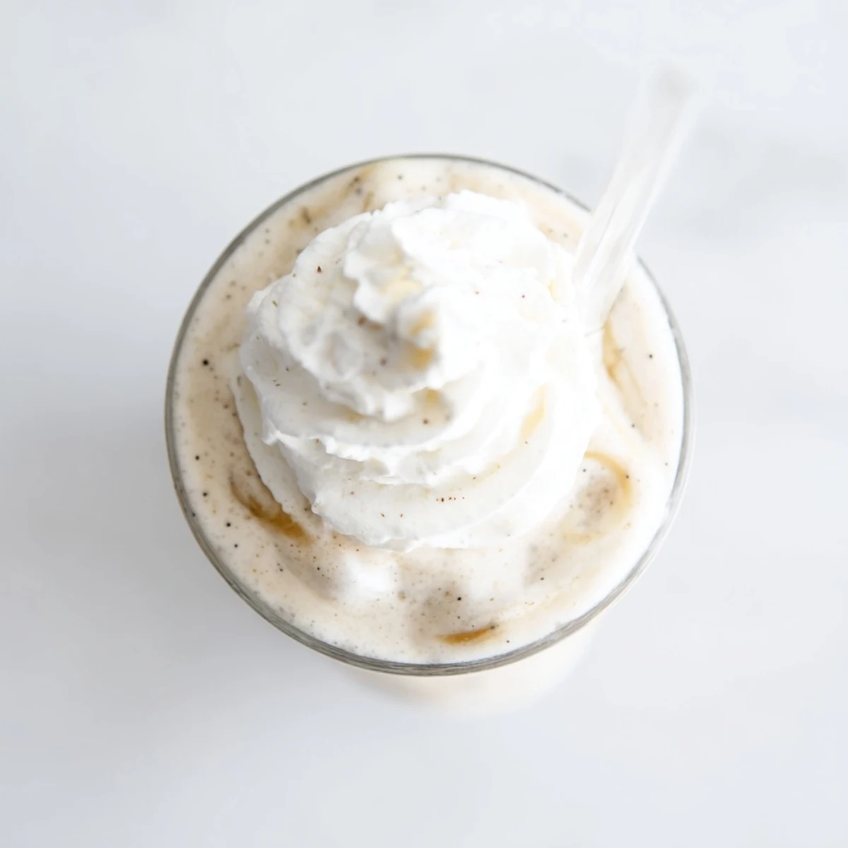 Cool Vanilla Bean Frappuccino with speckled vanilla bean seeds beside fresh ingredients on a marble counter.