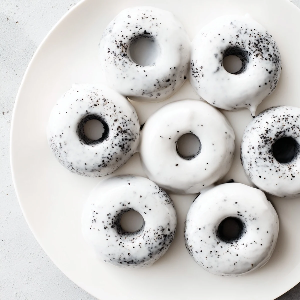 A plate of Black Sesame Mochi Donuts is drizzled with sweet glaze and dusted with extra sesame seeds, ready to eat.