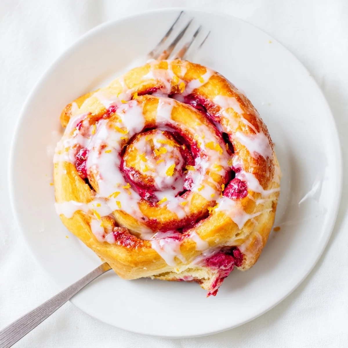 Golden Raspberry Cinnamon Rolls With Lemon Glaze on a ceramic plate, ready for a cozy brunch serving.