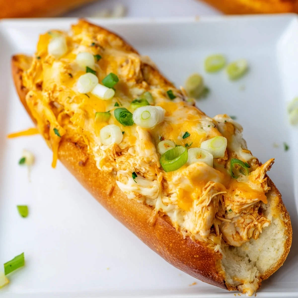 Golden brown French bread holds a generous stuffed Cheesy Buffalo Chicken filling, topped with fresh chopped green onions and vibrant parsley for a colorful appetizer.
