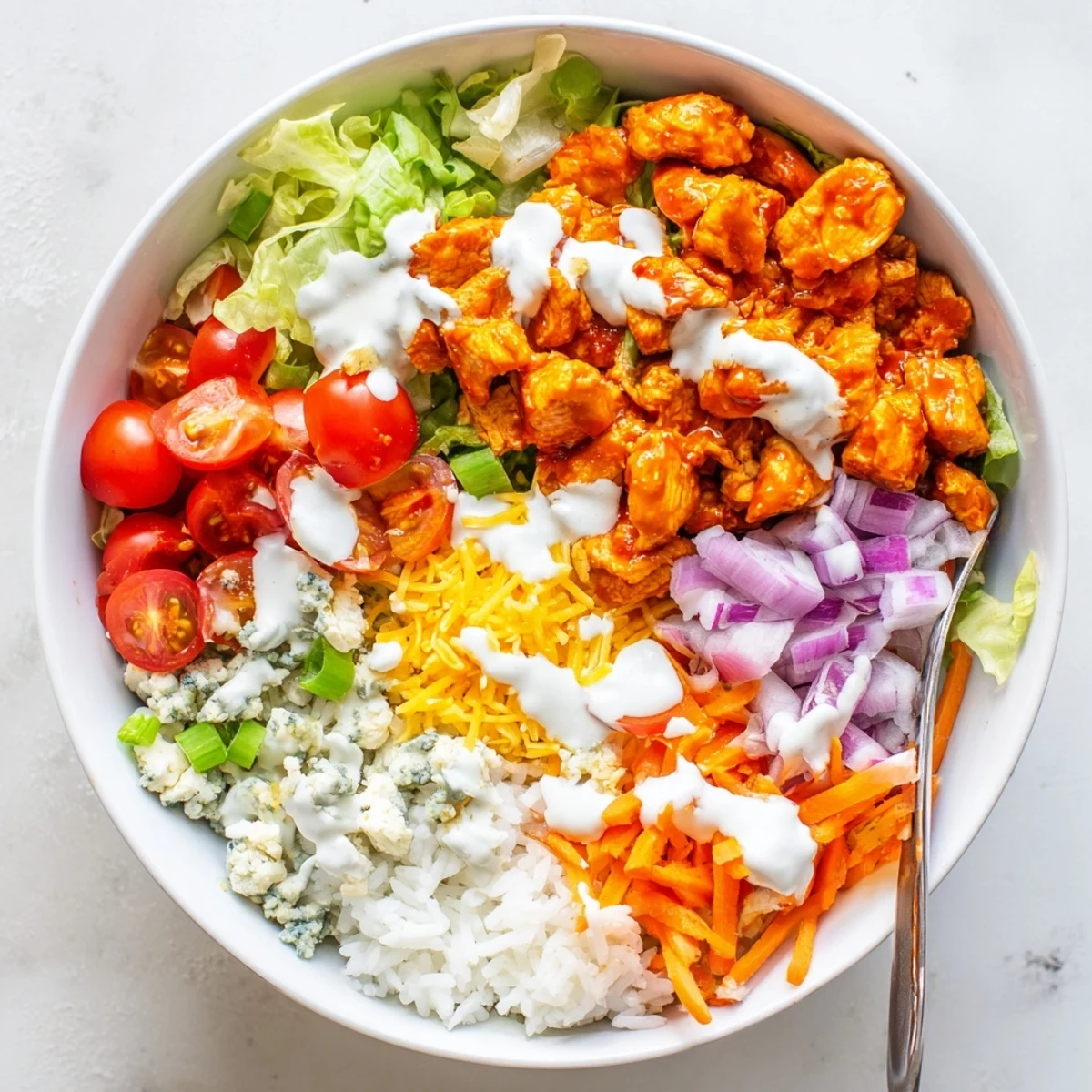 Creamy ranch drizzled Buffalo Chicken Bowls feature spicy tender chicken, crisp veggies, fluffy rice, and melted cheddar on a plate.