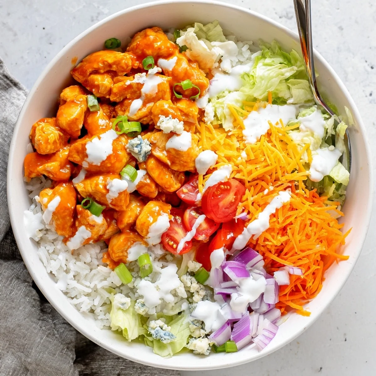 A colorful bowl of Buffalo Chicken Bowls with shredded lettuce, tomatoes, carrots, green onions, and blue cheese for a hearty meal.