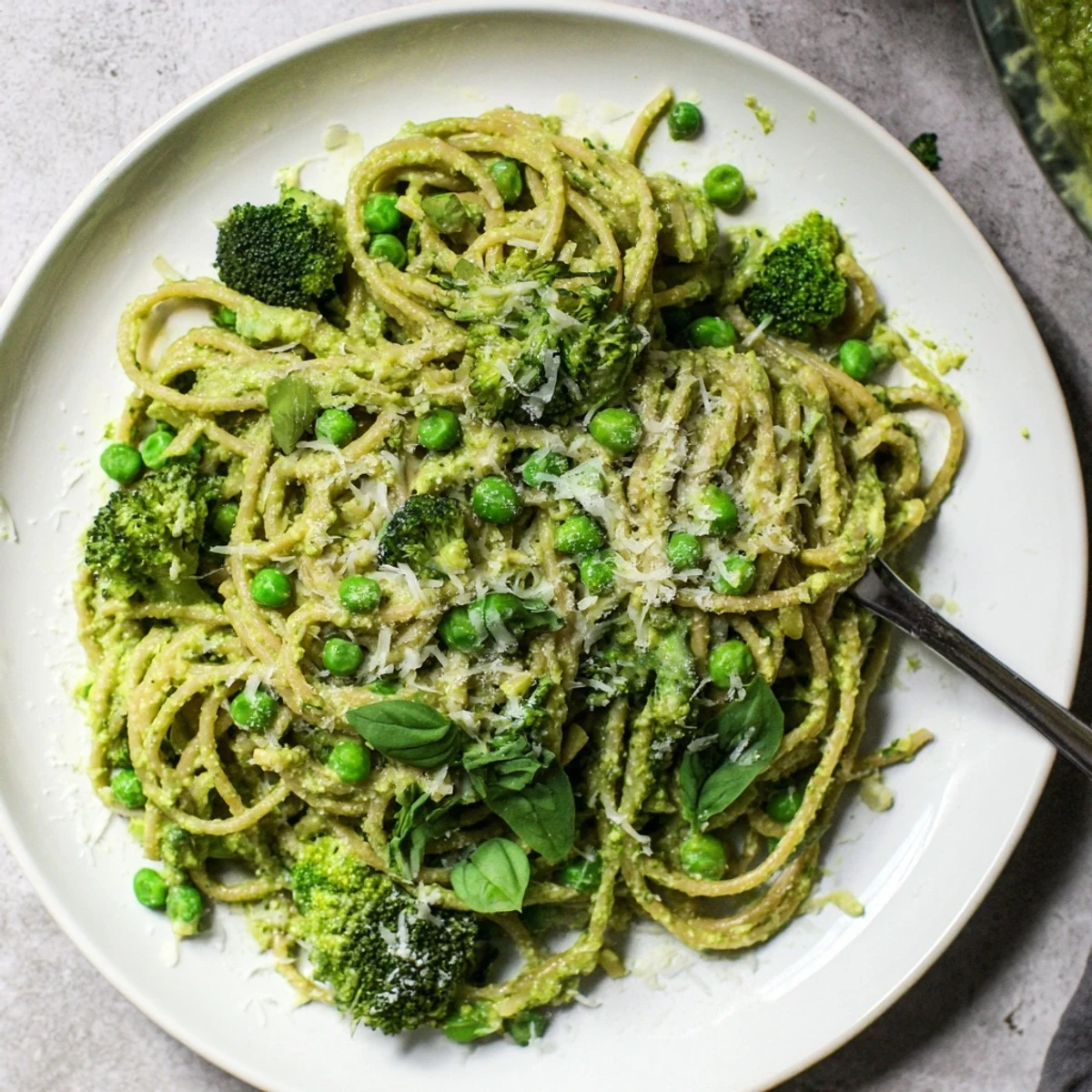 A close-up of Veggie Smuggler Avocado Pasta tossed with steamed broccoli and peas on a rustic wooden table.
