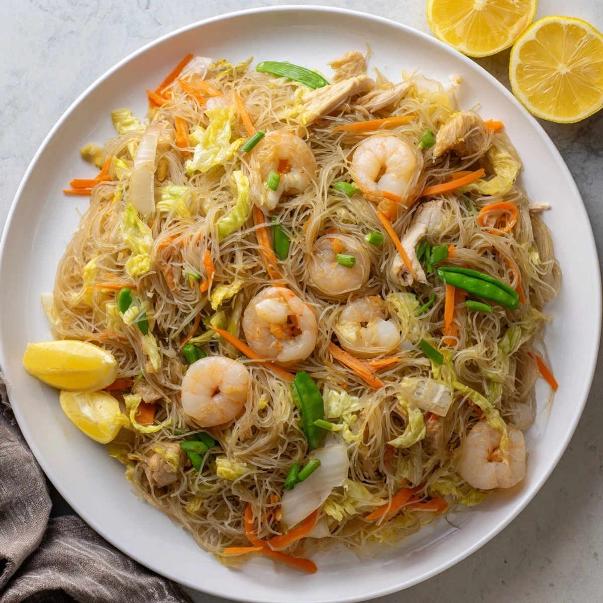 Rustic wooden serving board piled high with Filipino pancit bihon featuring rice vermicelli, protein, and vibrant vegetables ready for family-style dining
