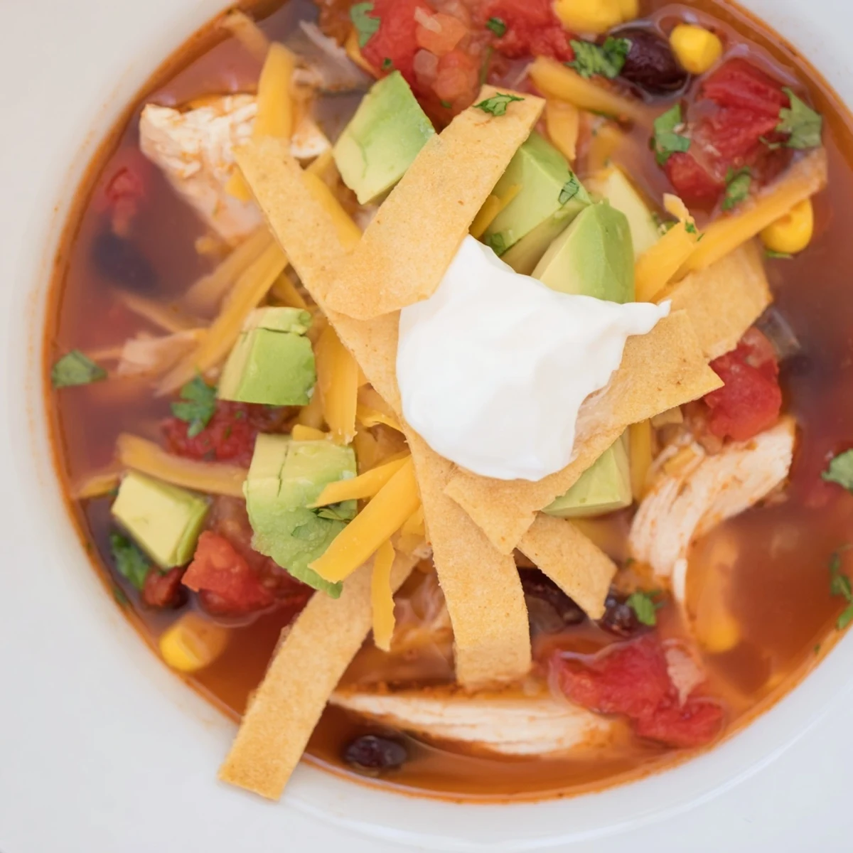 Steamy classic chicken tortilla soup garnished with creamy avocado, shredded cheese, and zesty lime wedges