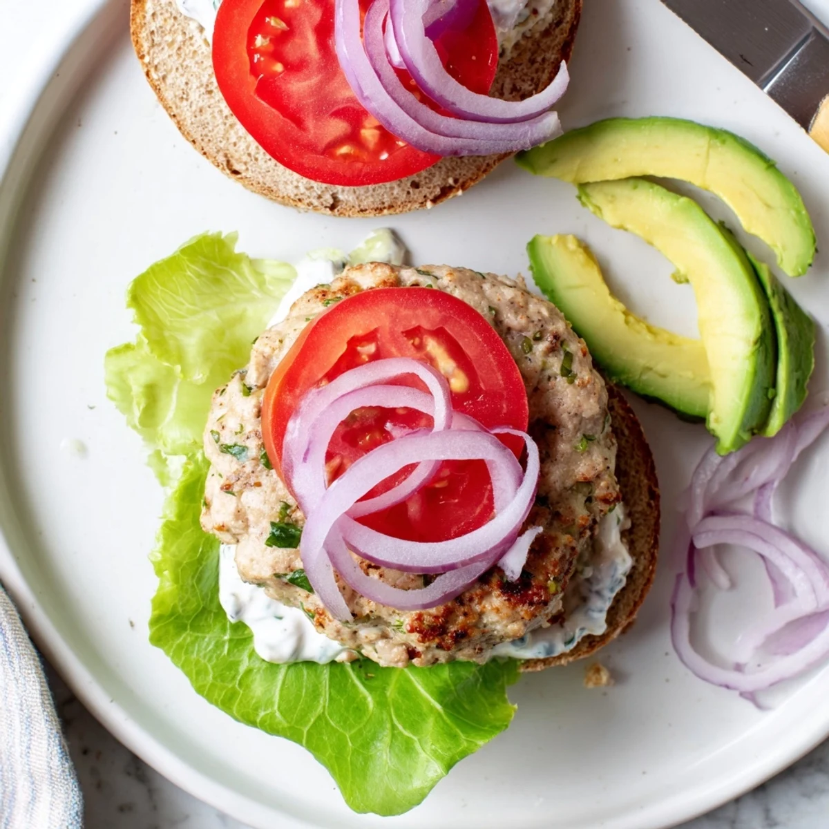 Juicy healthy high protein burger on toasted whole wheat bun with fresh tomato, crisp lettuce, and creamy Greek yogurt sauce