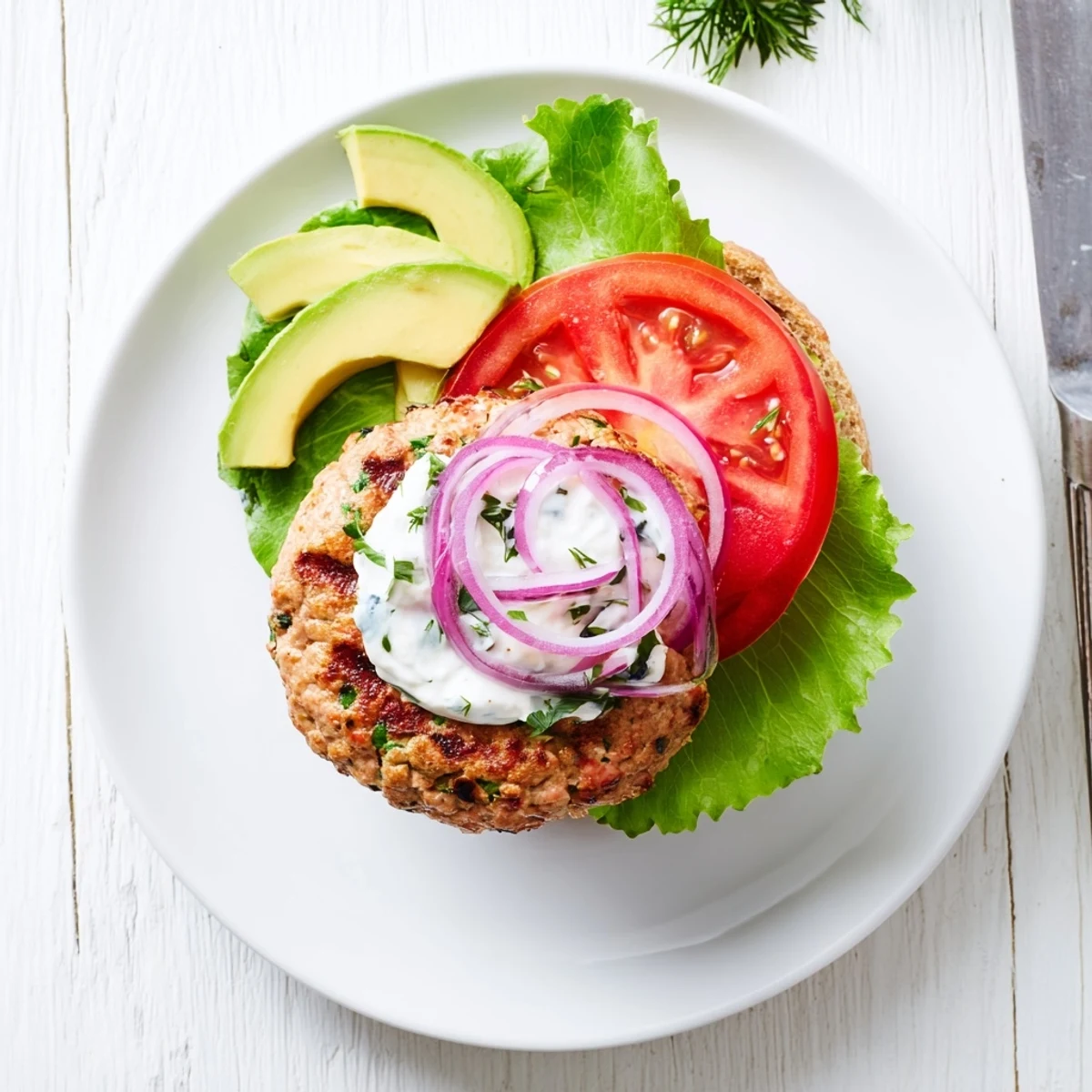 Golden brown healthy high protein burger patty stacked between a sesame bun with ripe avocado slices and red onion rings