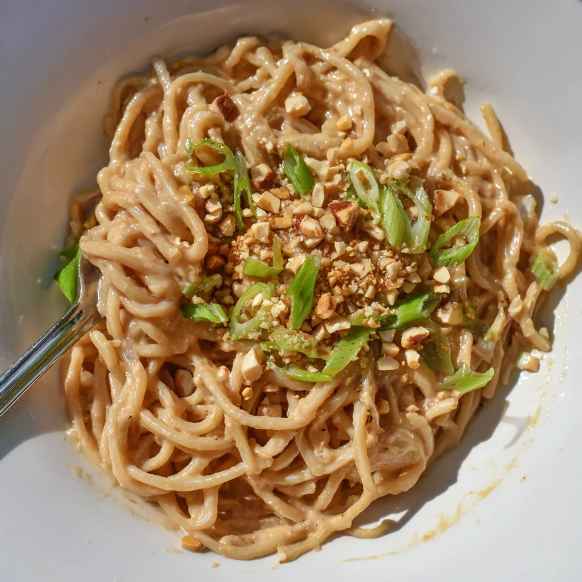Bowl of sticky peanut butter noodles coated in creamy peanut sauce with crushed peanuts and green onion garnish