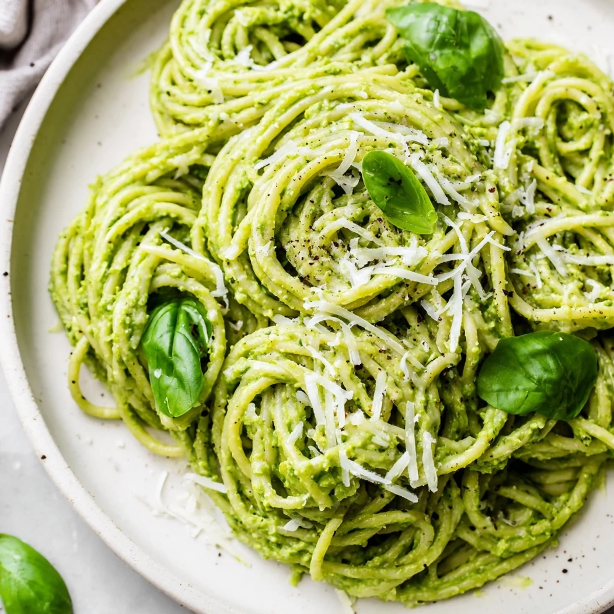 Creamy avocado spinach basil pesto coats al dente spaghetti noodles with vibrant green sauce and grated Parmesan cheese topping