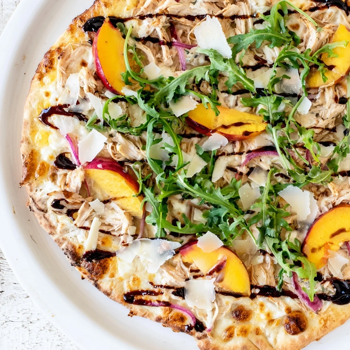 Summer-inspired pizza featuring juicy peaches, tender chicken, creamy ricotta, peppery arugula, and sweet balsamic reduction