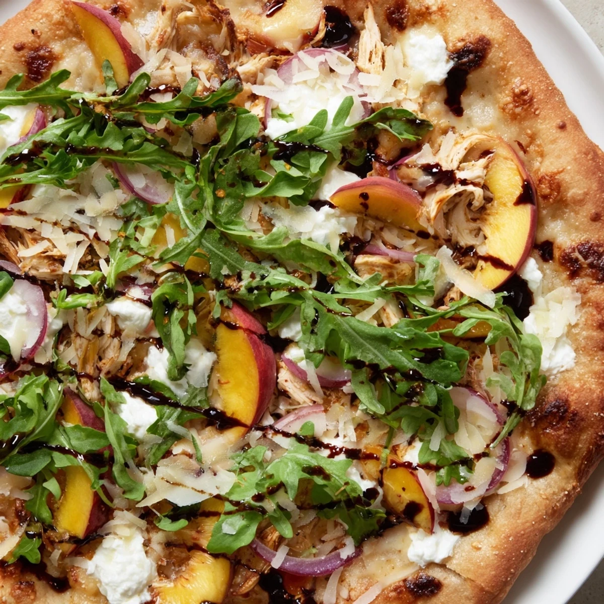 Slice of chicken and peach pizza with ricotta cheese, arugula topping, and balsamic glaze on golden baked crust