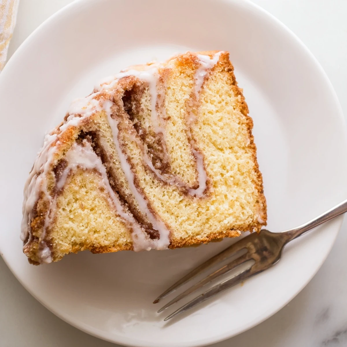 Warm cinnamon roll cake slice showing marbled cinnamon swirls under a sweet powdered sugar glaze