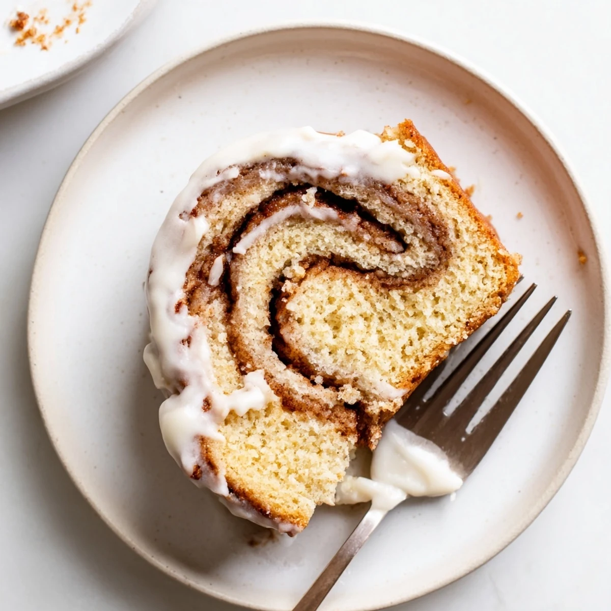 Soft buttery cake swirled with cinnamon sugar ribbons topped with silky vanilla glaze on a white plate