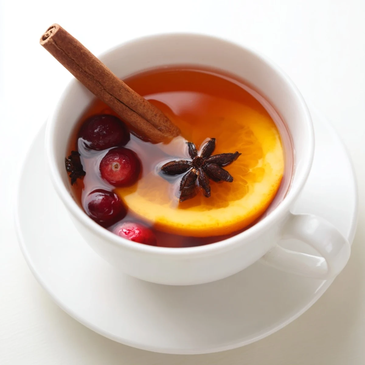 Steaming cup of Orange Cranberry Tea garnished with fresh orange slices and floating cranberries