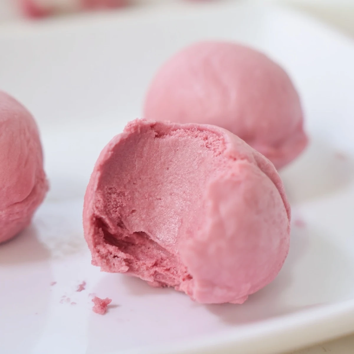 Close-up of bite-sized vegan strawberry mochi ice cream with smooth pink ice cream center peeking through soft translucent mochi skin.