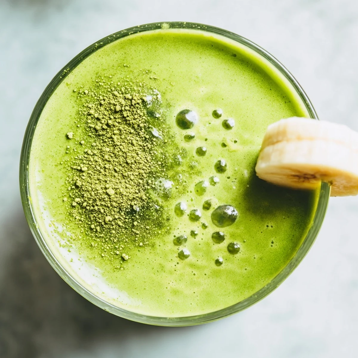 Thick vibrant green banana matcha smoothie blended with ice and chia seeds in a tall serving glass