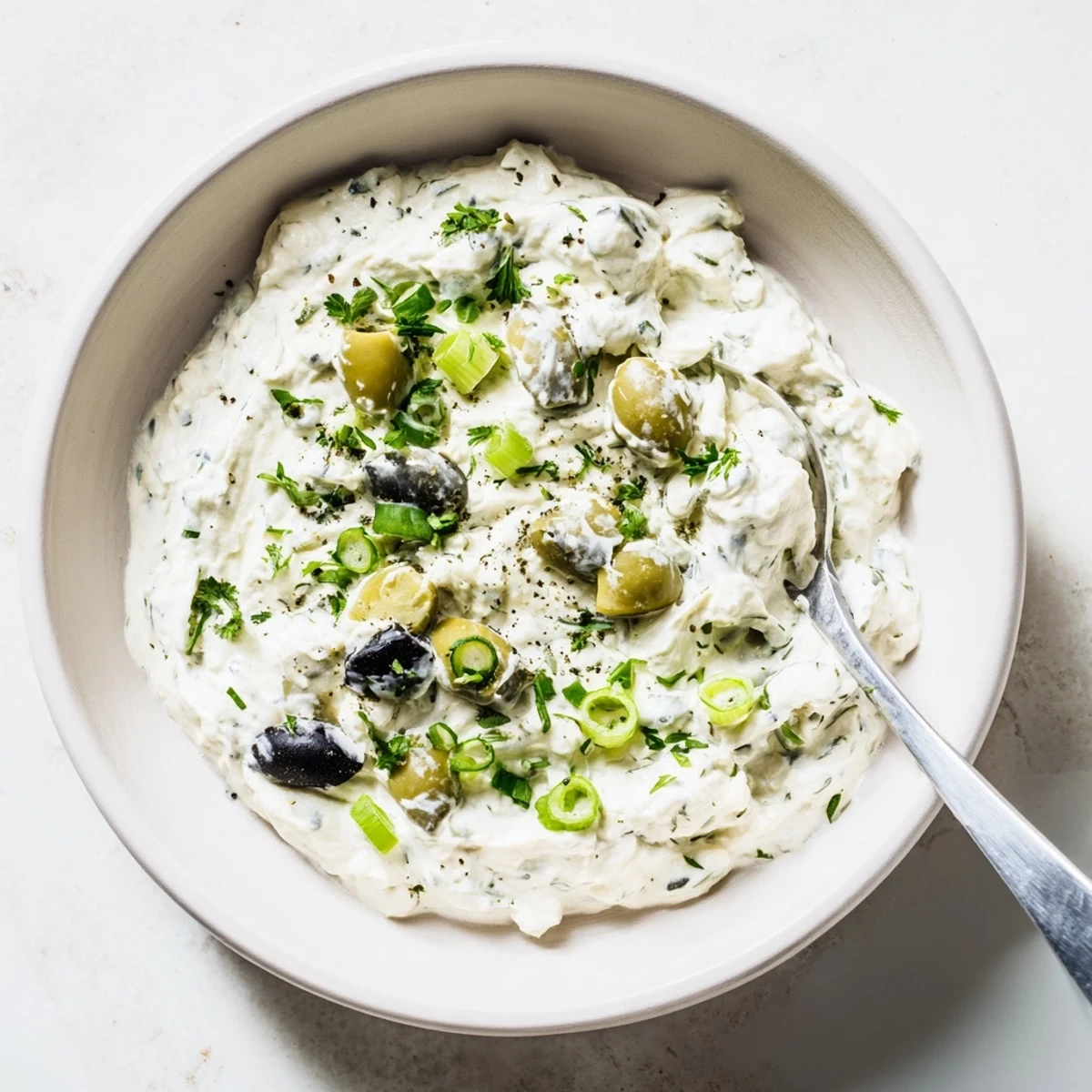 Cream cheese olive dip with chopped green and black olives in a white serving bowl