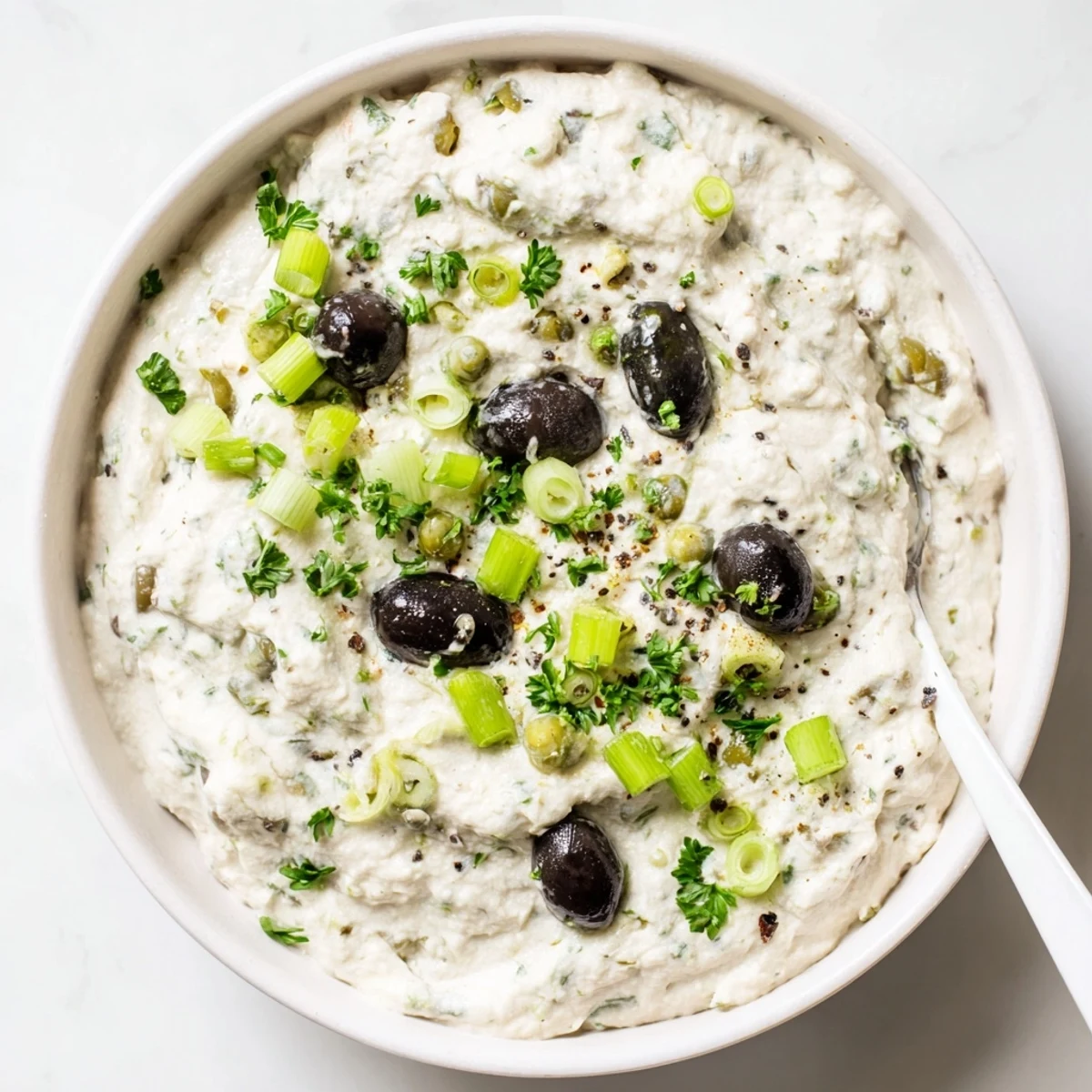 Creamy olive appetizer spread topped with fresh parsley and served with crispy crackers