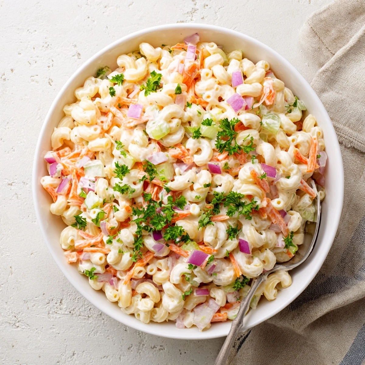 Colorful bowl of tangy and creamy macaroni salad loaded with crisp red bell peppers, diced celery, and shredded carrots in a rich mayonnaise dressing