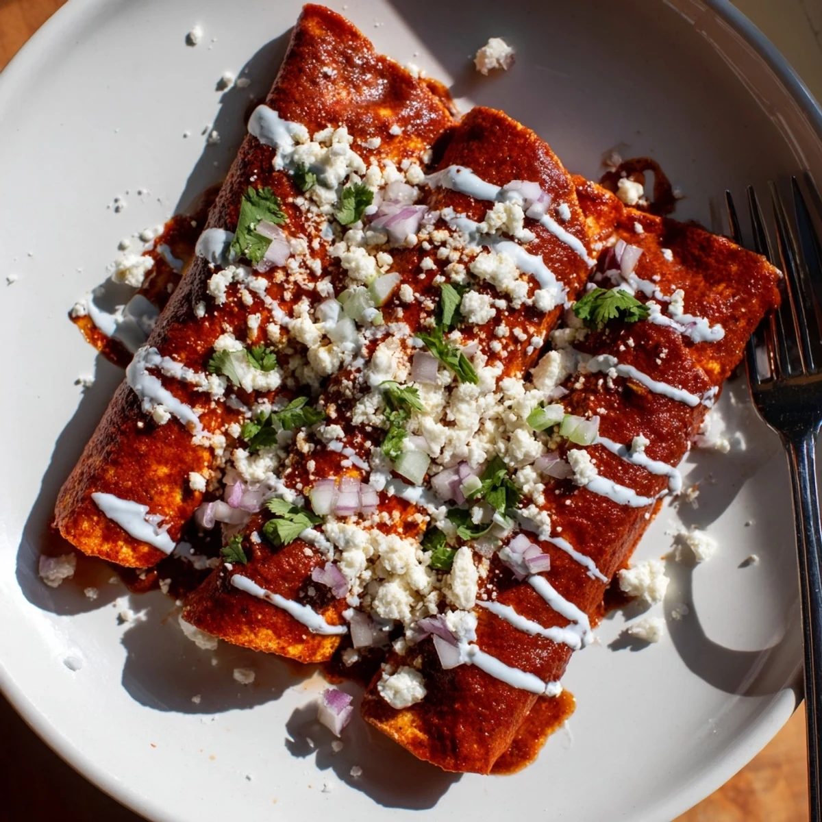 Warm entomatadas folded and smothered in vibrant red tomato sauce with creamy Mexican crema drizzle