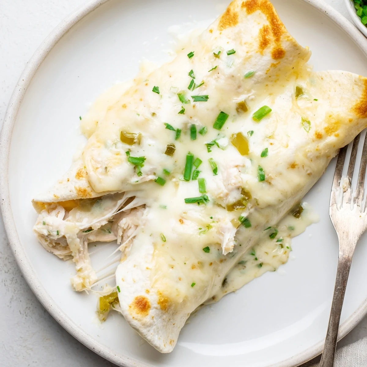 A stack of Creamy White Chicken Enchiladas sliced to show cheesy, saucy filling