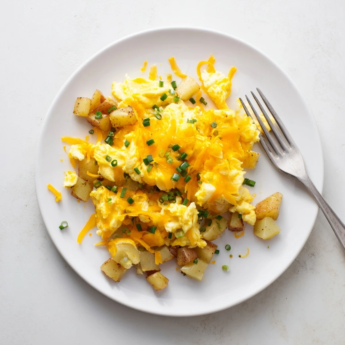 Hearty breakfast bowl of cheesy potato egg scramble topped with fresh green onion garnish