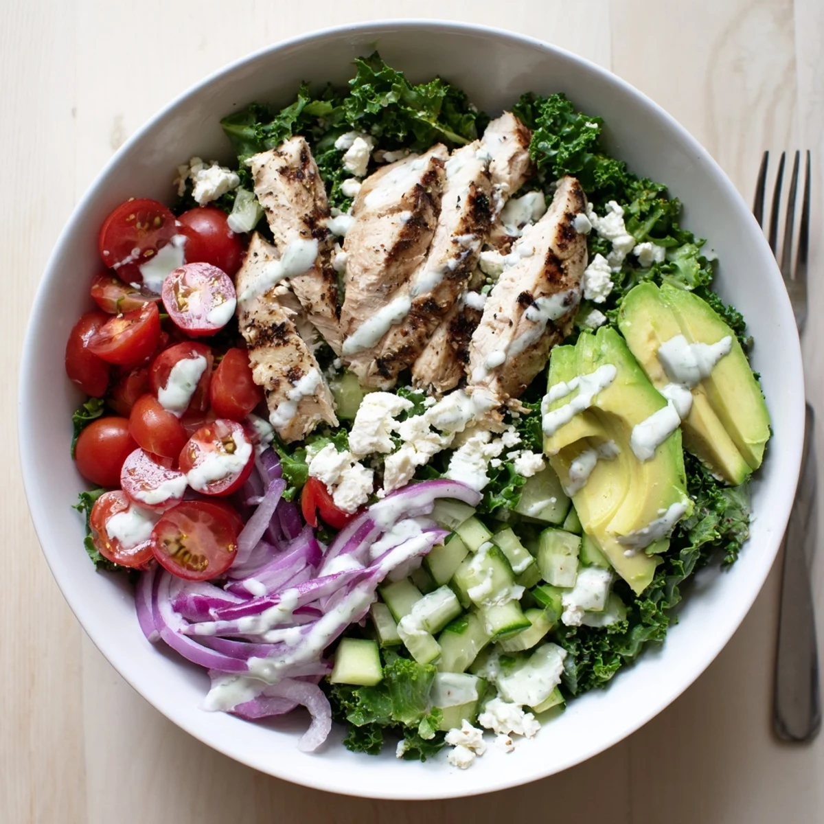 Colorful marinated kale and chicken bowl with fresh vegetables and creamy yogurt drizzle