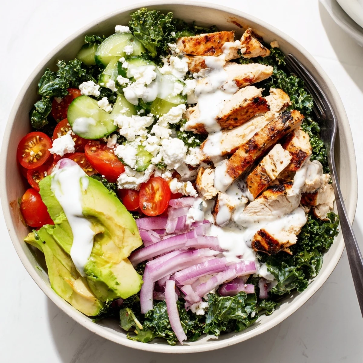 Sliced grilled chicken atop massaged kale with tomatoes avocado and zesty lemon dressing