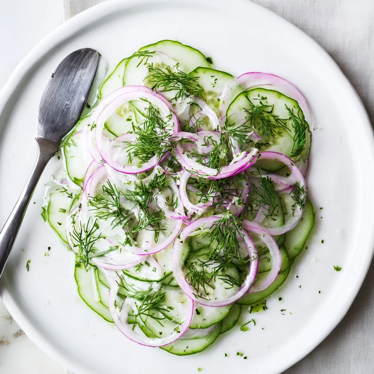 Glass bowl of refreshing cucumber salad topped with chopped fresh dill and zesty dressing
