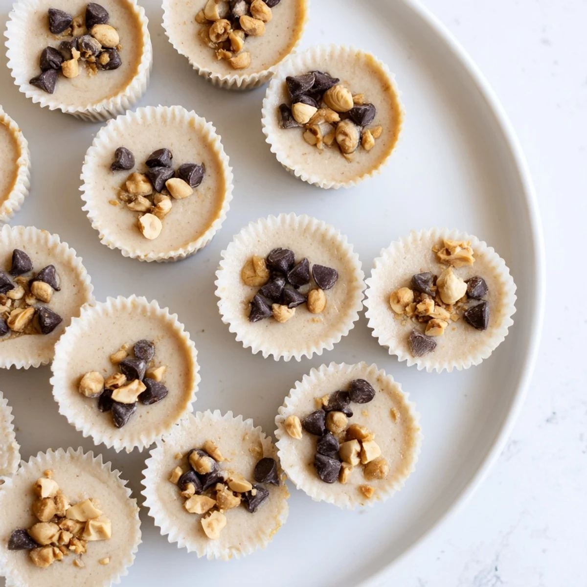 Creamy frozen peanut butter Greek yogurt bites topped with melted chocolate and crushed peanuts in a mini muffin tin
