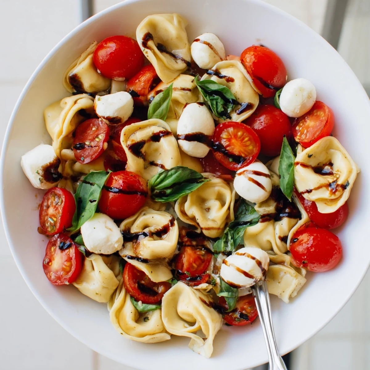 Colorful bowl of tortellini Caprese salad with cherry tomatoes, mozzarella, and fresh basil drizzled with balsamic glaze