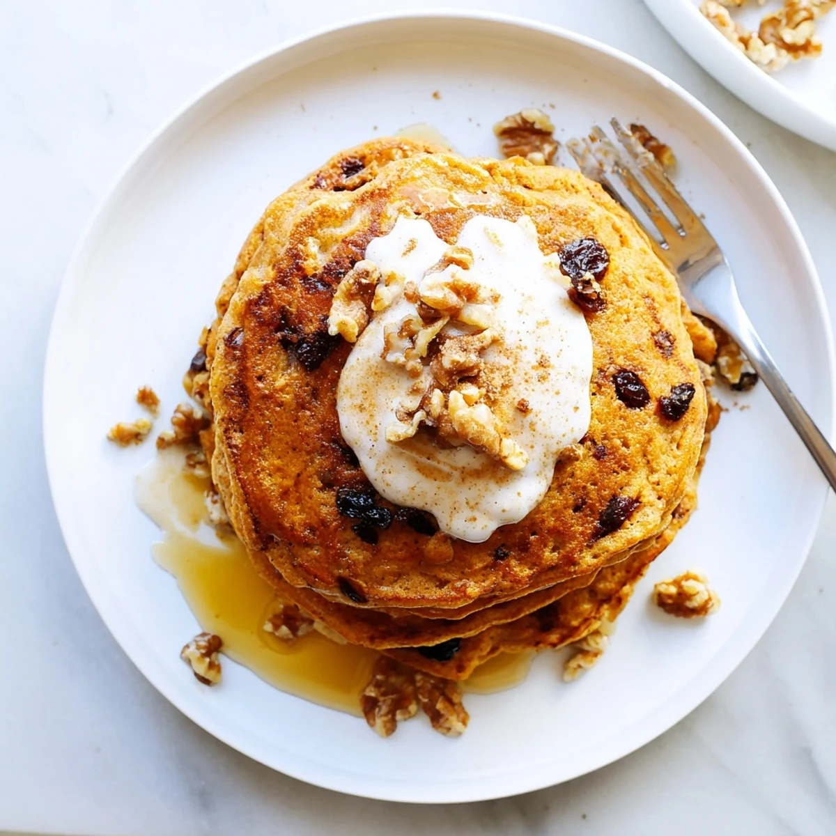 Golden stack of fluffy carrot cake pancakes topped with maple syrup and chopped walnuts