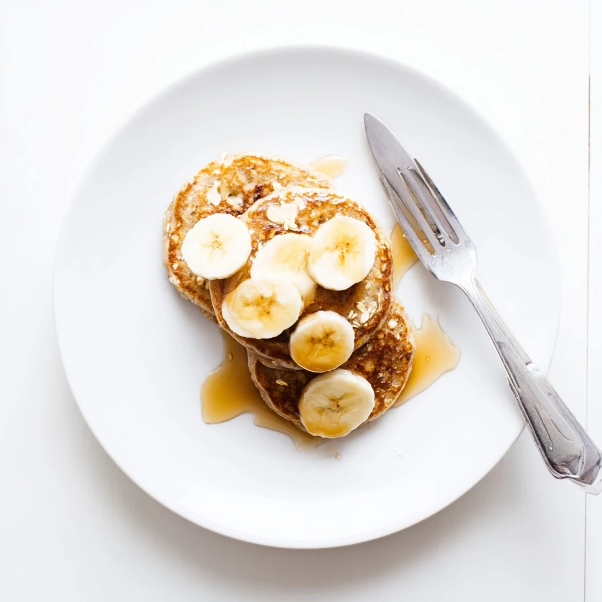 Golden stack of fluffy protein banana pancakes topped with fresh berries and maple syrup on a white plate