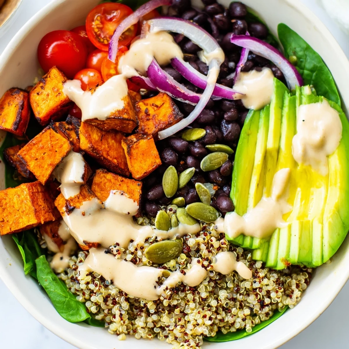 A vibrant sweet potato bowl drizzled with creamy tahini dressing and toasted pepitas