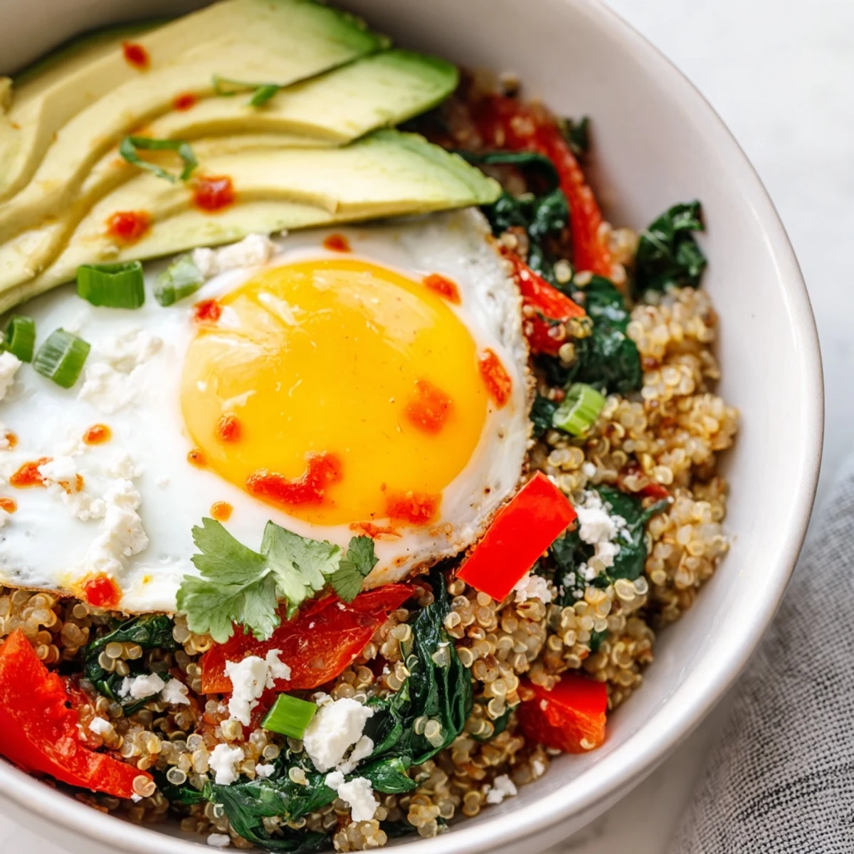 Warm savory quinoa breakfast bowl garnished with creamy avocado, crumbled feta, and fresh herbs