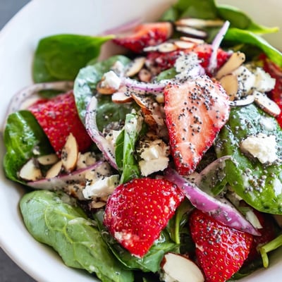 Savory poppy seed dressing drizzled over a vibrant strawberry spinach salad with red onion and feta.  